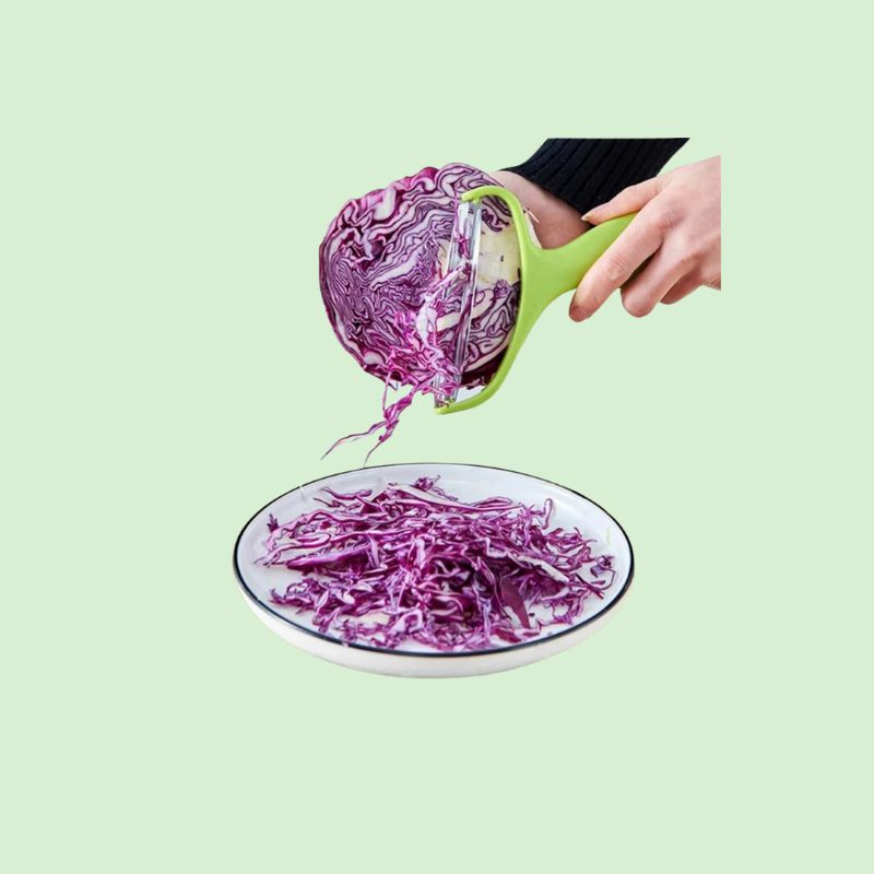 Éplucheur en acier inoxydable en train de râper du chou rouge, illustrant la facilité et l’efficacité du produit en cuisine.
