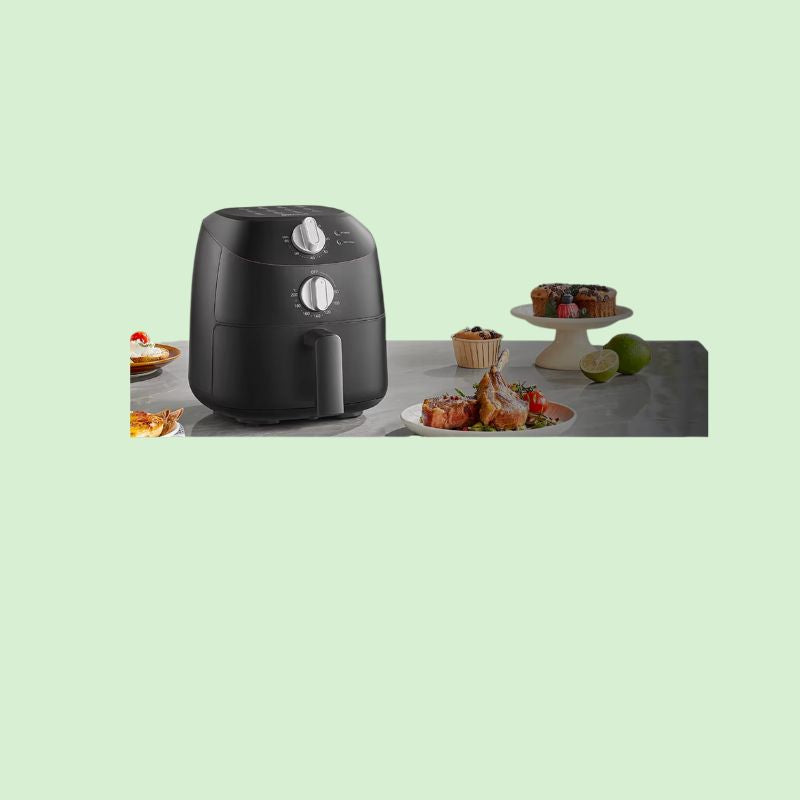 Friteuse à air 2 litres sur plan de cuisine avec différents plats autour : viande, cakes et autres aliments