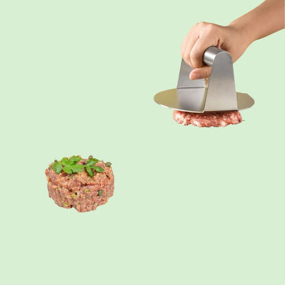 Presse à burger en inox en train de presser un steak haché à côté d’un autre steak haché