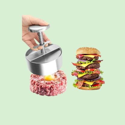 Presse à hamburger en inox antiadhésive posée sur un steak haché, avec un burger prêt à côté.